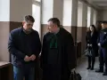Mężczyzna w todze prawniczej rozmawia z oskarżonym. W tle policjant i kobieta, być może świadkowie w sprawie o znęcanie.