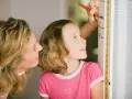 Mama mierzy córkę, która z zaciekawieniem patrzy na miarkę. Czyżby zastanawiała się, dlaczego dziecko nie rośnie tak szybko, jak by chciała?