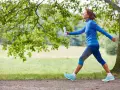 Femme souriante en tenue de sport bleue, profitant de 30 minutes de marche rapide par jour dans un parc verdoyant.