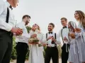Świadek na ślubie otwiera szampana, podczas gdy panna młoda i jej drużba trzymają kieliszki.
