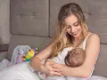 Uśmiechnięta mama karmi piersią dziecko. W tle pluszowe zabawki. Nakładki na pierś do karmienia mogą pomóc w tym intymnym momencie.