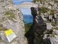 Himmelspforte am Schafberg: Ein Felsentor mit Holzinschrift, das den Blick auf einen See freigibt. Ein Wanderer steht im Durchgang.