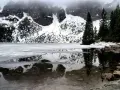 Morskie Oko zimą, zamarznięte, z odbiciem ośnieżonych gór i ciemnych drzew w przejrzystej wodzie.
