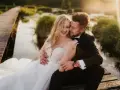Uśmiechnięta para młoda na sesji ślubnej. Panna młoda ma piękną fryzurę i koronkową suknię, pan młody w eleganckim garniturze.
