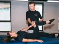 Un kinésithérapeute guide une patiente dans un exercice pour soulager la cruralgie. Elle est allongée sur une table de massage, une jambe pliée, l'autre tendue.