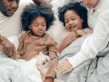 Familie kuschelt im Bett, um sich mit Kindern zu entspannen. Ein kleiner Hund liegt zwischen ihnen.