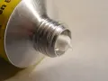 Tubo di alluminio con crema bianca che fuoriesce, mostrando diversi tipi di silicone.