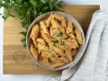 Penne alla vodka cremose e invitanti, guarnite con prezzemolo fresco, servite in una ciotola su un tagliere di legno con il logo MasterChef.