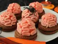 Gruselige Halloween-Nachspeise: Kekse mit Gehirn-förmiger rosa Glasur, dekoriert mit einer Spinne. Kerzen leuchten im Hintergrund.