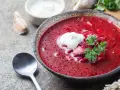 Aromaticzny barszcz czerwony domowy z łyżką śmietany i natką pietruszki, obok czosnek i chleb.