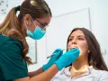 Dentystka w masce i rękawiczkach bada zęby pacjentki. To nie jest wyrywanie 8, ale rutynowa kontrola.