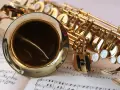 Ein glänzendes Musikinstrument, ein Saxophon, liegt auf Notenblättern. Seine goldene Oberfläche reflektiert das Licht.