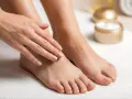 A woman's hands gently touch her feet, which are covered in exfoliating granules, hinting at a Johnson's foot soap recipe for soft skin.