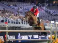 Cavalier en tenue rouge saute un obstacle lors d'une compétition équestre, visant la victoire à la **equestrian cup**.