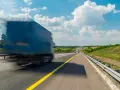 Niebieska ciężarówka w ruchu na autostradzie pod błękitnym niebem z chmurami.
