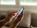 Dłonie trzymają smartfon, na ekranie którego wyświetla się niebieski kolor. Zastanawiasz się, jak sprawdzić ile lat ma telefon?