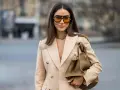 Mujer con gafas naranjas y blazer camel. Su bolso marrón y gargantilla dorada complementan el look, creando un estilo chic para combinar camel y azul.