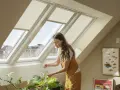 Donna annaffia piante sotto un lucernario fisso, godendosi la luce naturale che illumina l'ambiente.