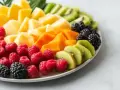 Kolorowa taca z owocami: maliny, jeżyny, kiwi, mango i papaja. Idealny sposób, jak podać owoce na imprezie, zachwycając gości!