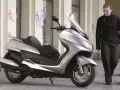 Srebrny skuter Yamaha Majesty 400, symbol miejskiej elegancji, obok kobiety w ciemnej kurtce.