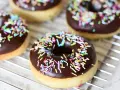 Färska, hembakade donuts med chokladglasyr och färgglatt strössel ligger på ett galler. Perfekt för att baka donuts!