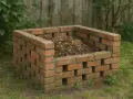Solidny kompostownik murowany, wypełniony resztkami organicznymi, stoi na trawniku wśród zieleni.