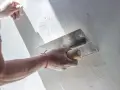 Ręka z kielnią wygładza świeżą gipsowaną ścianę.