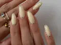 Modne paznokcie wzory galeria: kremowe migdałki z błyszczącymi kropkami. Delikatny manicure, który przyciąga wzrok.