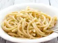 Pici, pasta fatta a mano con un'origine antica, servita in una ciotola bianca con una forchetta.