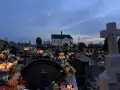 Cmentarz nocą, pełen płonących zniczy i kwiatów. W oddali kościół, a na niebie księżyc. Modlitwa świętej Gertrudy w ciszy zadumy.