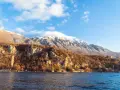 Góry i jezioro w Macedonii. Warto zobaczyć malownicze wybrzeże z domkami i ośnieżone szczyty w tle.
