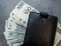Czarny portfel z plikiem banknotów 100 zł. Czy to oszczędności na przyszłość, czy może zapłata za podatek od emisji CO2?