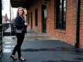 Mujer con outfit de camisa azul a rayas, pantalones negros y zapatos de tacón.