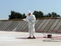 Pracownik w białym kombinezonie natryskuje białą masę na dach. To nowoczesna metoda izolacji, która zastępuje tradycyjną **styropapę**.