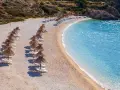 Rządki parasoli i leżaków na kamienistej plaży, obok krystalicznie czystej, turkusowej wody. To jedna z najpiękniejszych plaż w Europie.