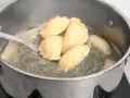 Pierogi gotujące się w garnku, wyjmowane łyżką cedzakową.