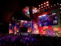 Kolorowa scena festiwalu Poland Rock 2026 z wielkim ekranem pokazującym publiczność. Tłum widzów wpatrzony w widowisko.