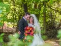 Uśmiechnięta para młoda w lesie, z bukietem kolorowych kwiatów. To ich protokół przedślubny, pełen radości i miłości.