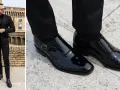 Uomo con vestito nero e camicia abbinata, indossa eleganti scarpe da abbinare in vernice nera.
