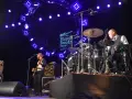 Un groupe joue du blues musique sous un grand cercle lumineux. Un bassiste à gauche, un batteur à droite.