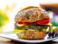 Deliciosa hamburguesa de espinacas con pan de semillas, queso, tomate y lechuga, servida en un plato blanco.