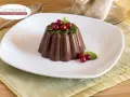 Budino al cioccolato decorato con ribes rossi e menta, servito su un piatto bianco.