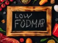 Na tablicy napis "LOW FODMAP". Wokół świeże produkty: mięso, ryba, pomidorki, cytryna, jajko, papryka, orzechy, jagody, szpinak.