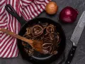 Cipolle in agrodolce caramellate in padella, pronte per essere gustate. Accanto, cipolle fresche e un coltello affilato.