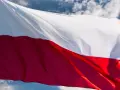Flaga biało-czerwona powiewa na wietrze na tle błękitnego nieba z chmurami.