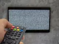 Ręka trzyma pilot dekodera, celując w ekran telewizora z zakłóceniami. Czas na naukę, jak sparować pilot dekodera z telewizorem.