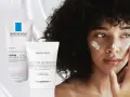 Eine Frau mit lockigem Haar trägt Gesichtscreme auf. Links sind zwei Tuben zu sehen, eine mit "Urea 10%" und eine mit "Urea Face Cream".