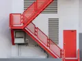 Nowoczesne schody wejściowe do domu w intensywnym czerwonym kolorze, prowadzące do czerwonych drzwi.