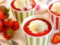 Vanilleeis mit Erdbeeren und Sahne in bunten Bechern. Frische Erdbeeren liegen daneben.