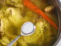 Łyżeczka soli czeka na dodanie do bulionu z kurczakiem i marchewką. Kiedy solić rosół? Najlepiej pod koniec gotowania, by doprawić go do smaku.